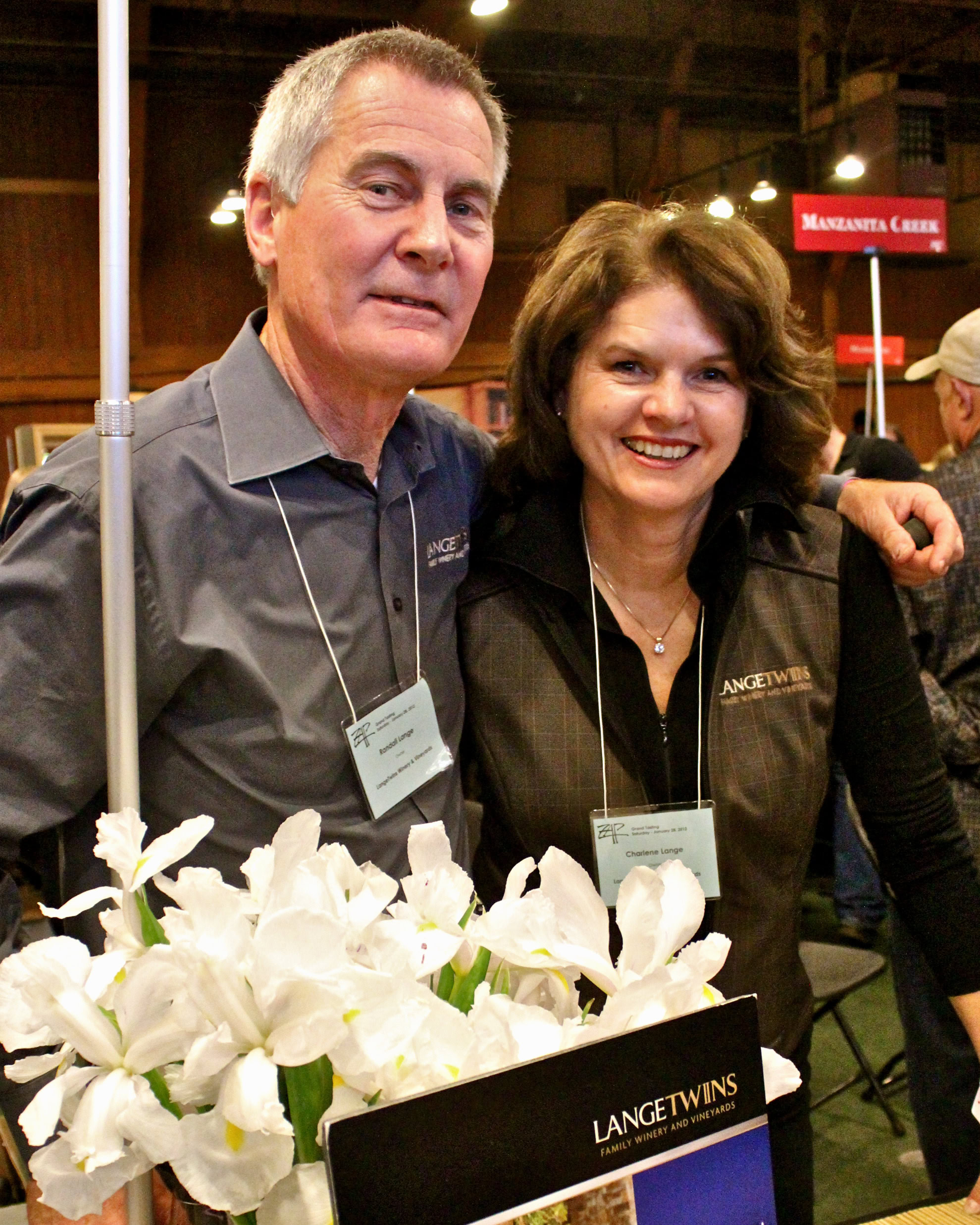 Two smiling individuals at a Lodi Winegrape Commission event, surrounded by wine industry professionals.