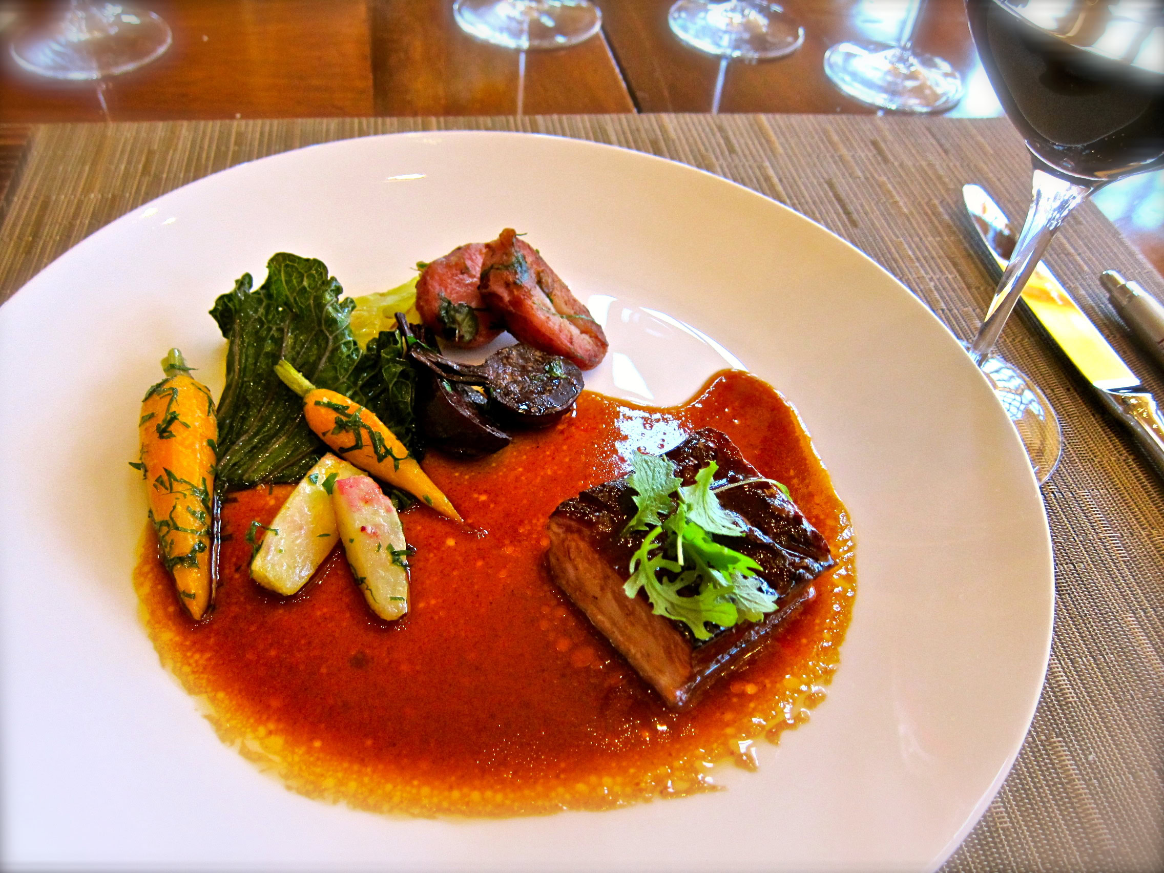 Elegant gourmet dish with vegetables and meat, served with red wine in a fine dining setting.