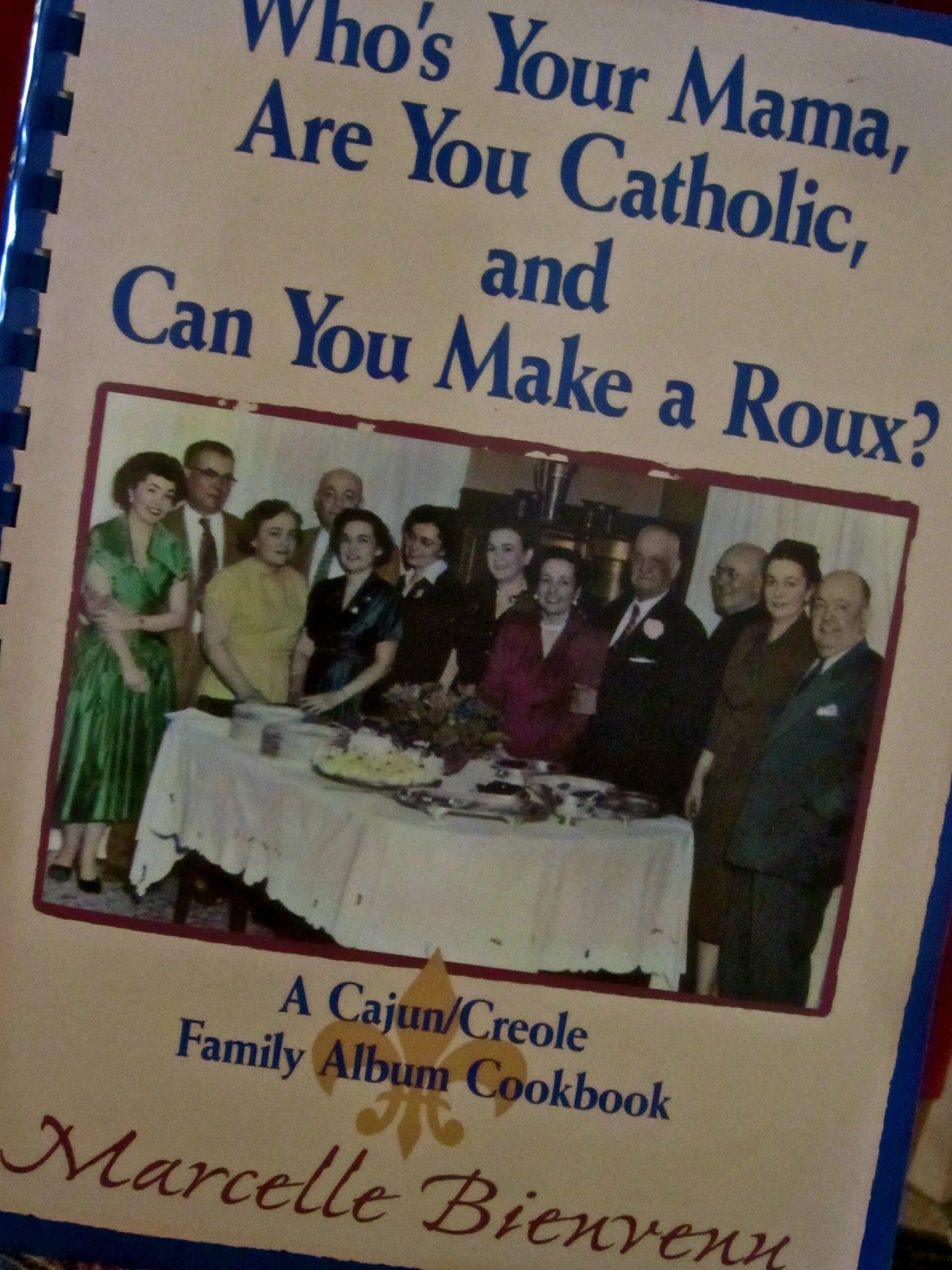 Group of people at a family cookbook event, with a table of food and drinks, in a community setting.