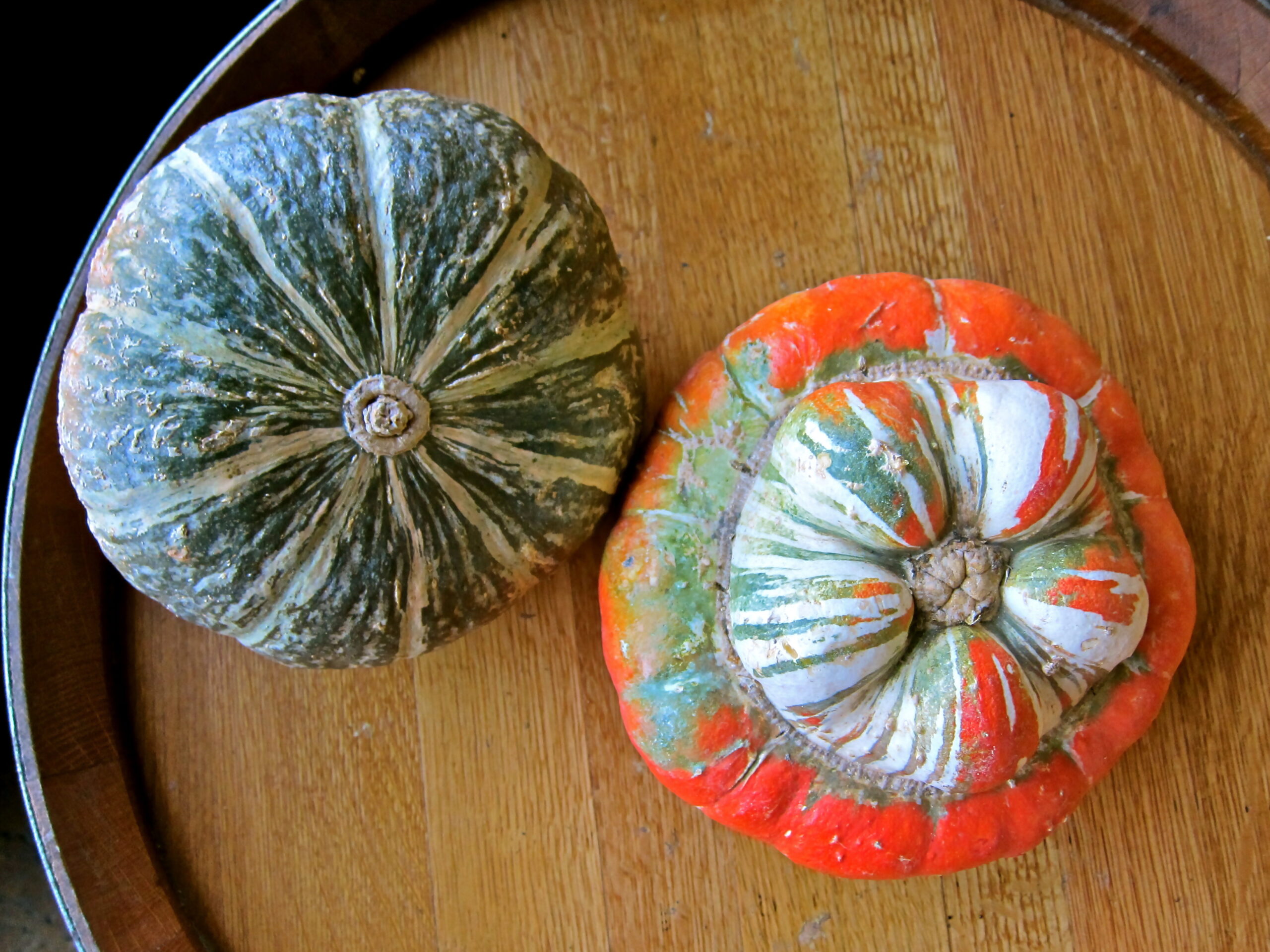Two decorative pumpkins on a wooden surface, representing fall harvest and seasonal produce.