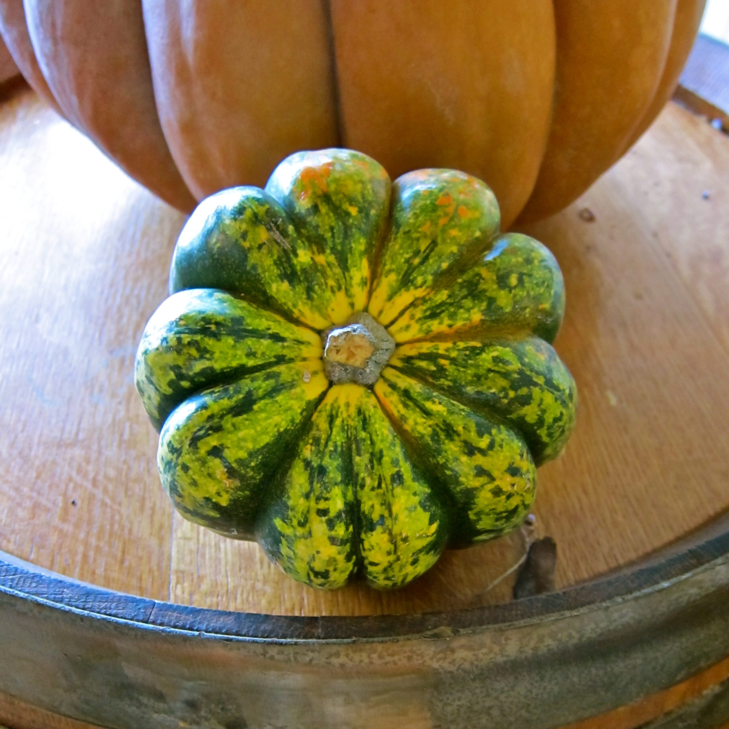 A vibrant, multicolored gourd with green, yellow, and orange hues on a wooden table.
