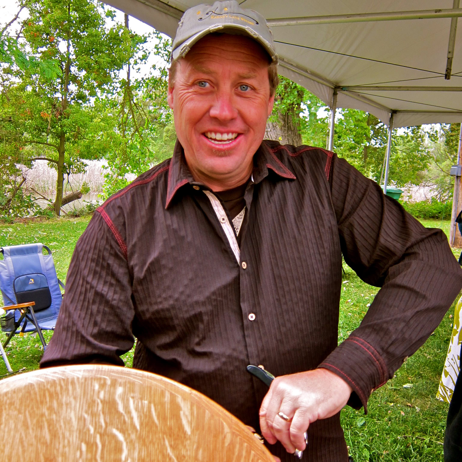Smiling man at Lodi Winegrape Commission event outdoors with trees and a tent in the background.