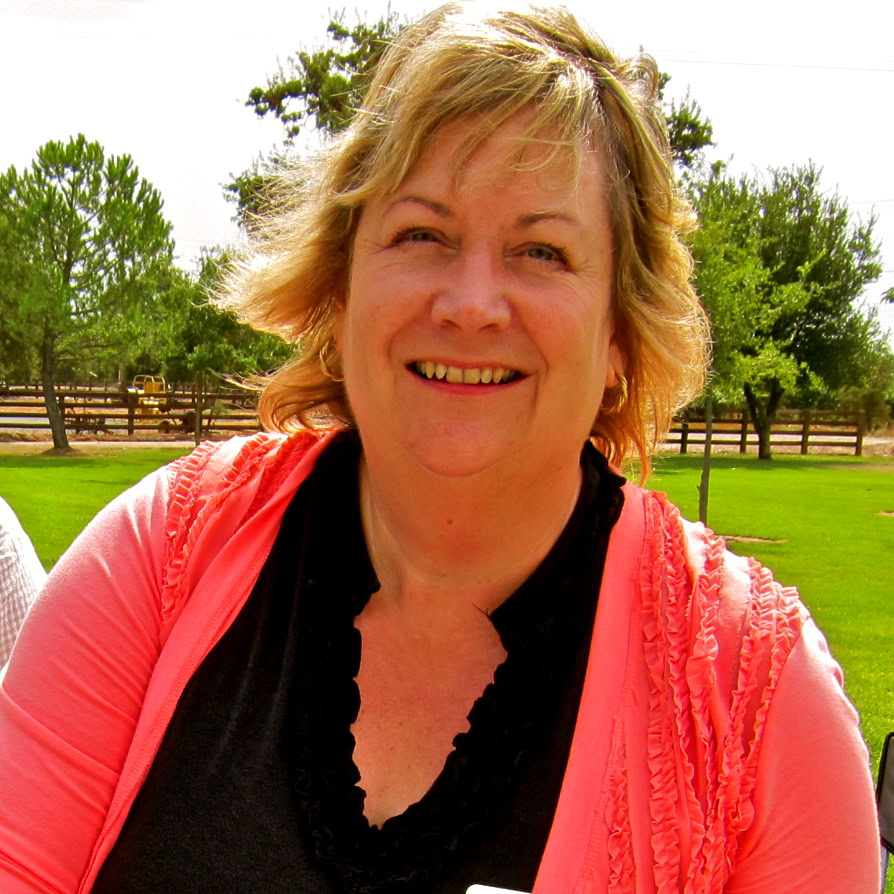 Smiling woman outdoors in Lodi, California, with vineyards and trees in the background.