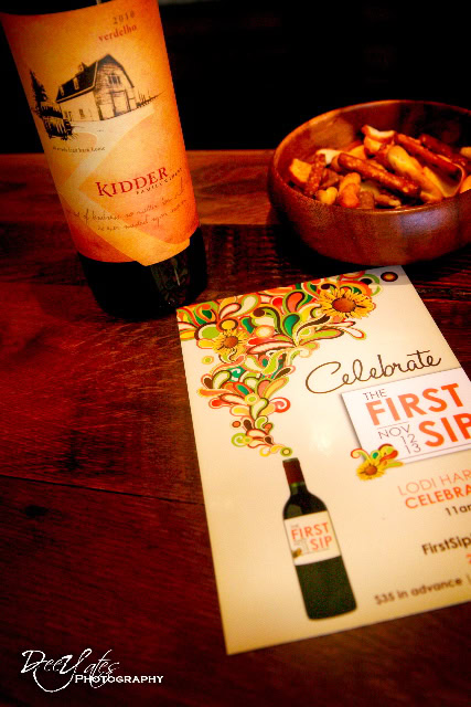 Lodi wine bottle, bowl of food, and promotional flyer for First Sip event on a wooden table.