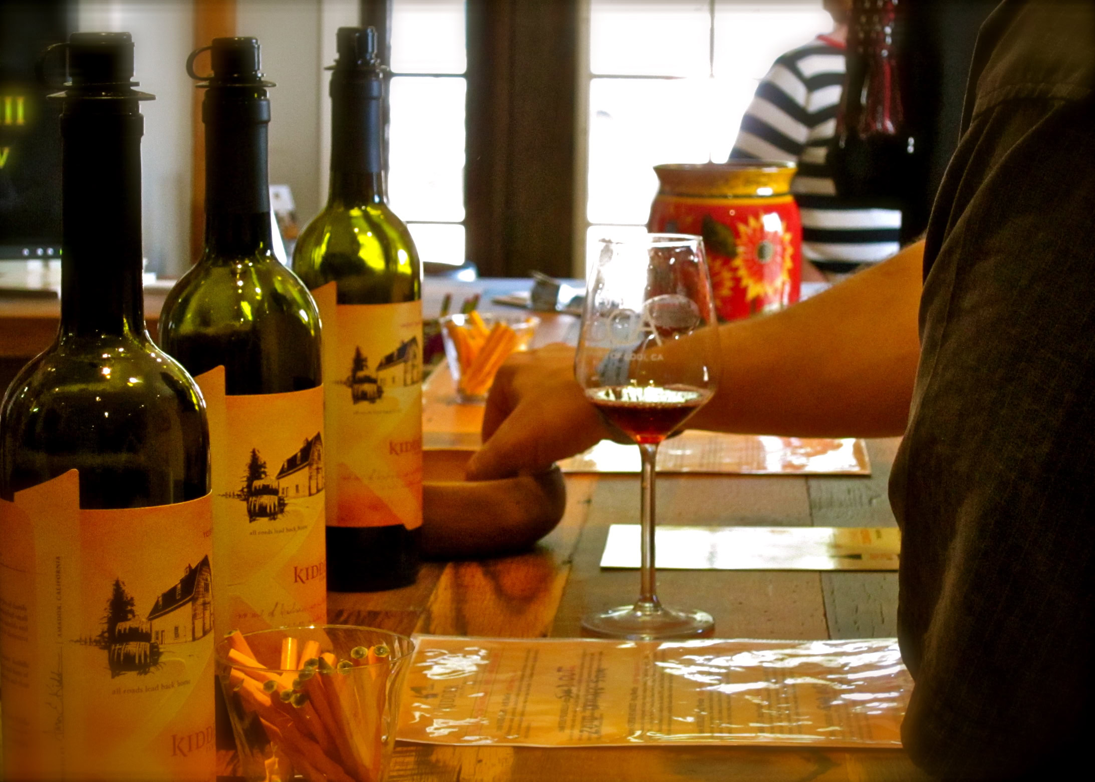 Wine tasting at Lodi Winegrape Commission with bottles and glasses on a rustic bar.