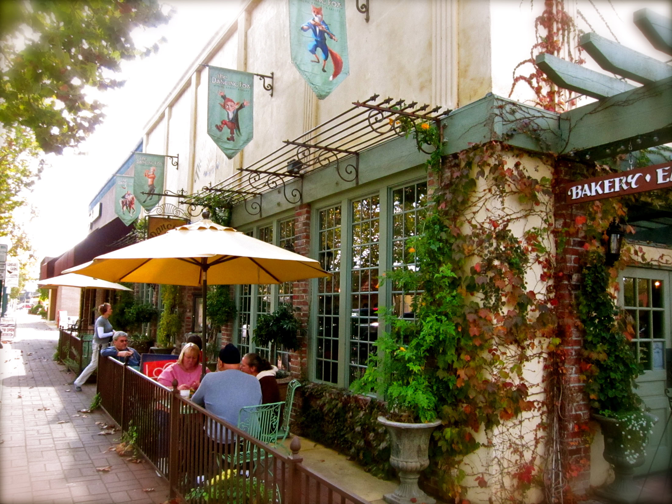 Outdoor cafe at a winery with patrons, banners, and lush greenery in Lodi, California.