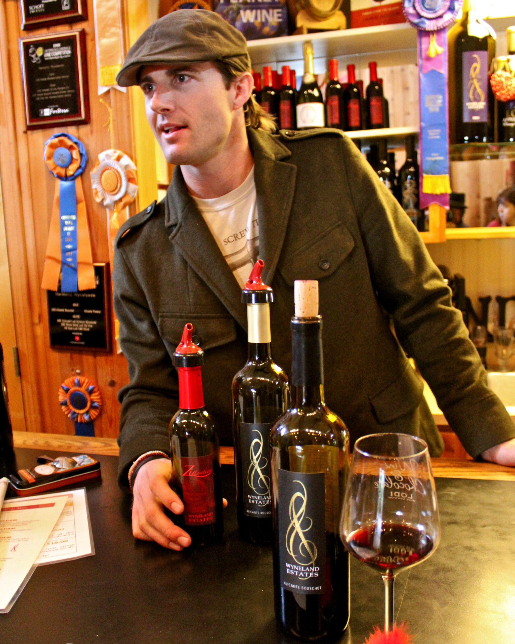 Man tasting wine at Lodi Winegrape Commission event with wine bottles and awards in background.