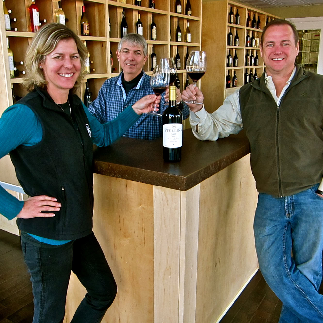 Three people enjoying wine tasting at Lodi Winegrape Commission with wine bottles and glasses.