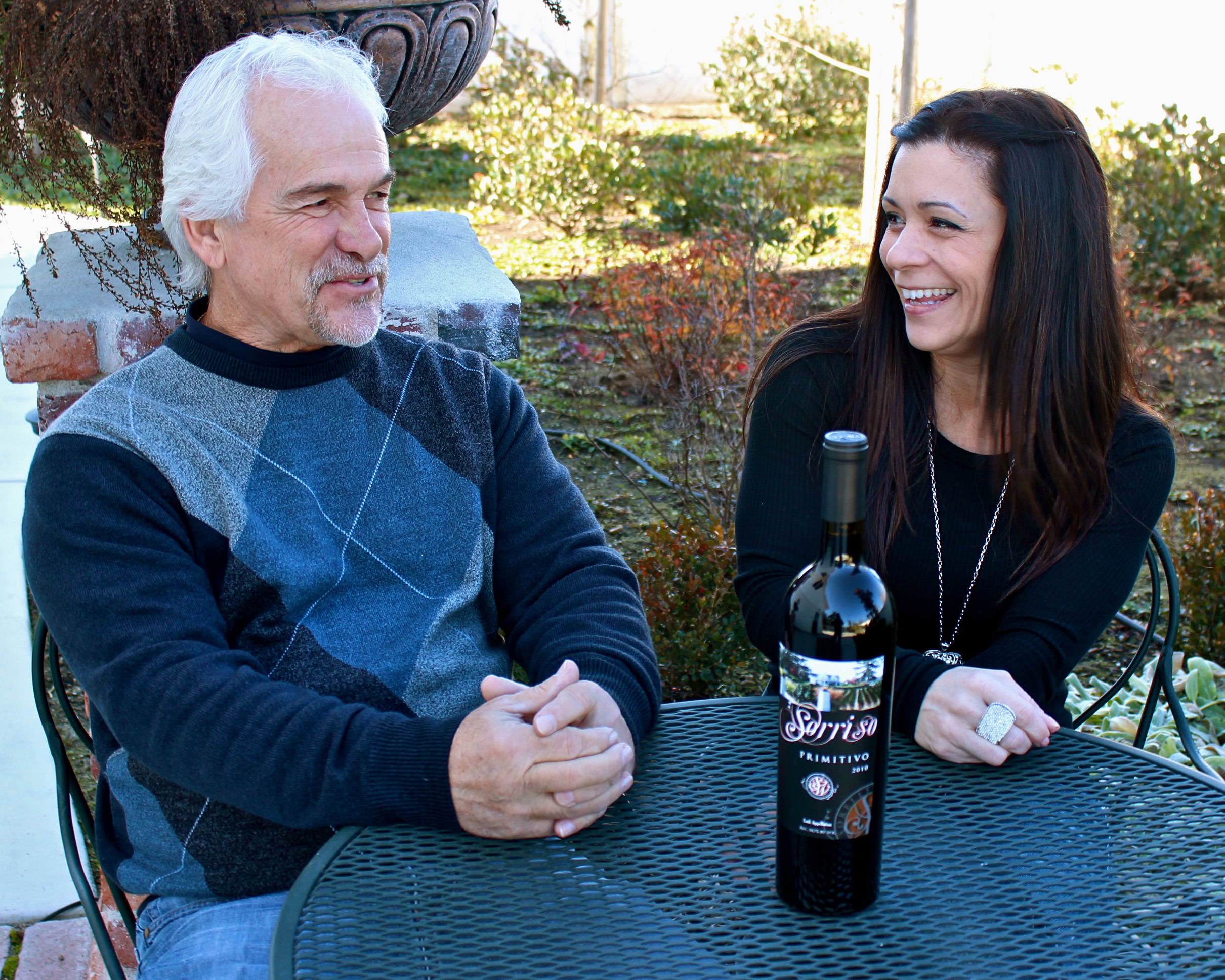 Two people enjoying wine tasting outdoors with a bottle of Lodi wine on the table.