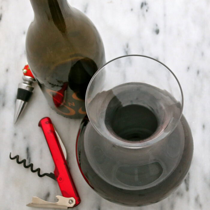 Close-up of a wine bottle and glass of red wine on a marble surface, with corkscrew and cork nearby.