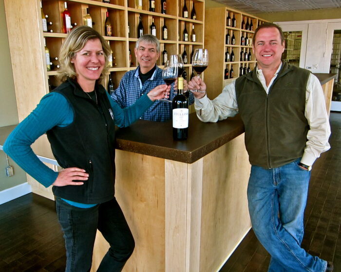 Three people enjoying wine tasting at Lodi Winegrape Commission with wine bottles and glasses.