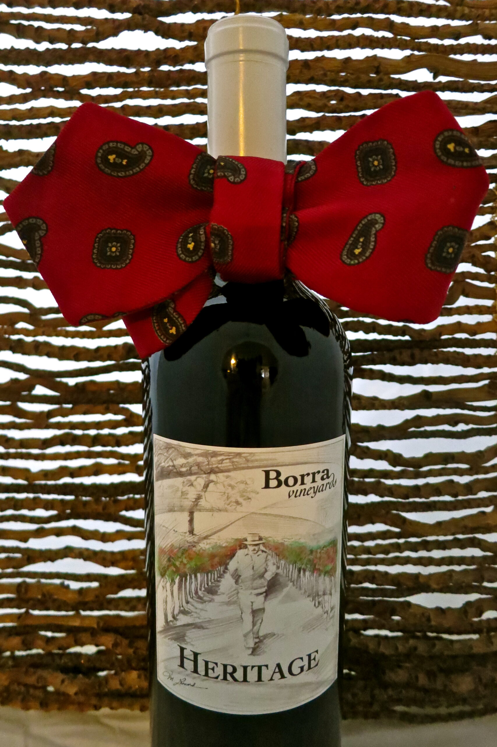 Heritage wine bottle from Borra Vineyards with a red bow, set against a woven background, showcasing Lodi wine heritage.