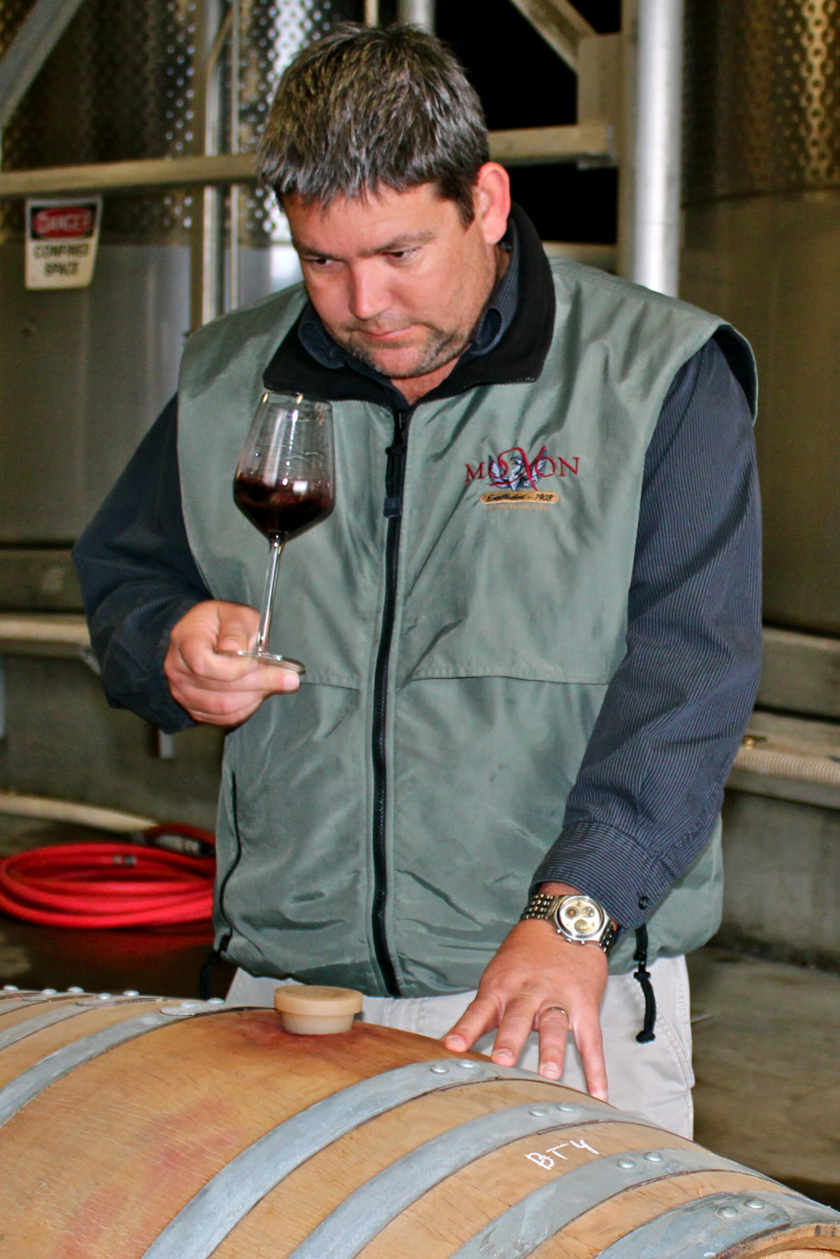 Man tasting wine from a glass while inspecting a wine barrel at a winery in Lodi, California.