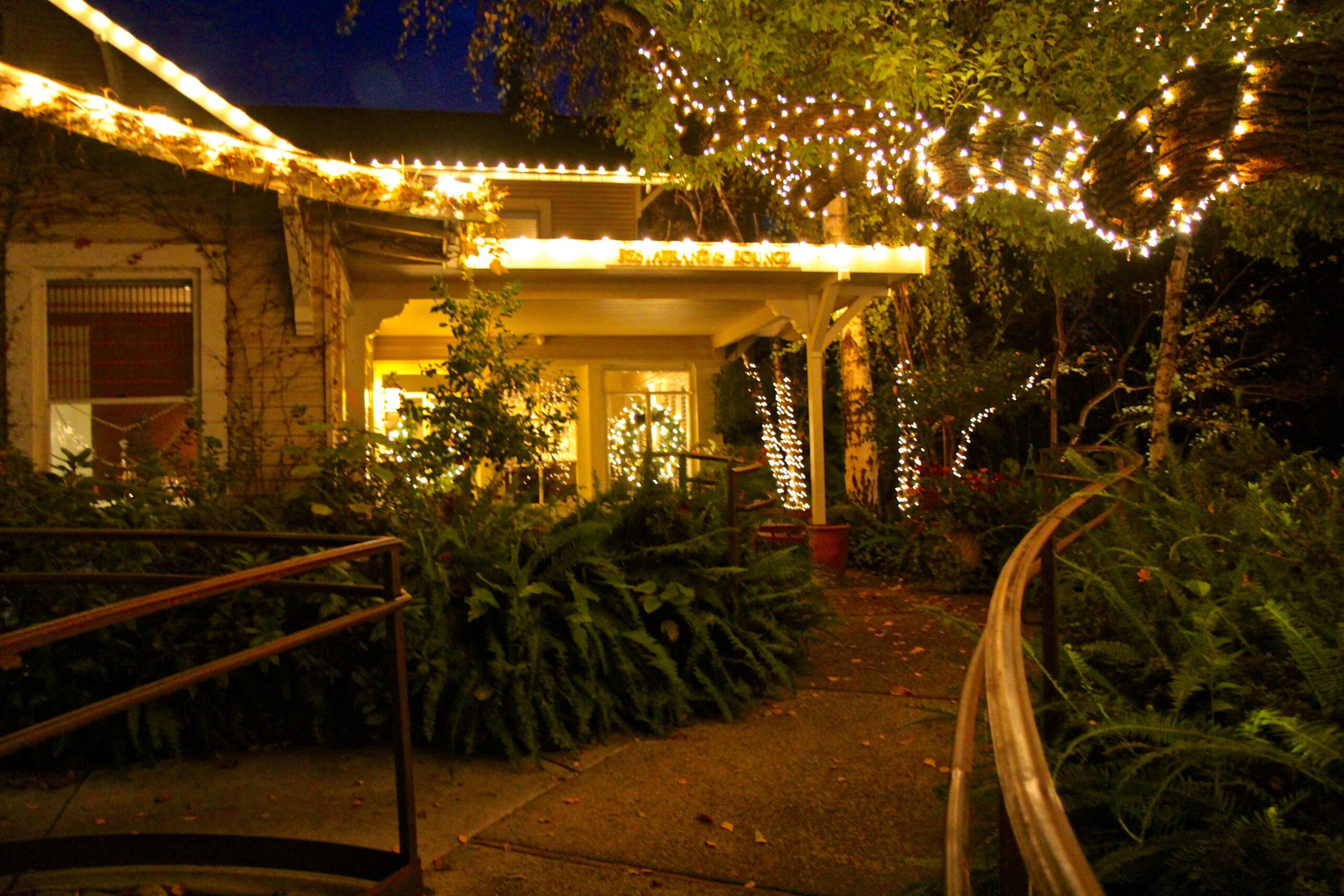 Night scene of a house decorated with string lights and surrounded by lush greenery, promoting Lodi wine region.