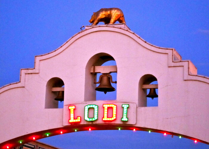 Lodi Winegrape Commission sign with colorful lights and a bell tower, featuring a golden bear statue on top.