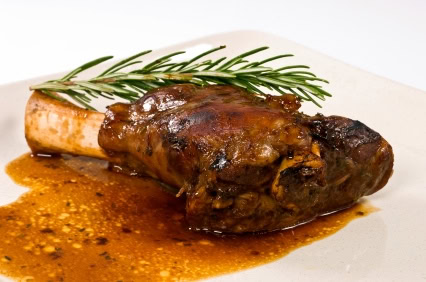 Close-up of a tender braised lamb shank garnished with rosemary on a white plate.