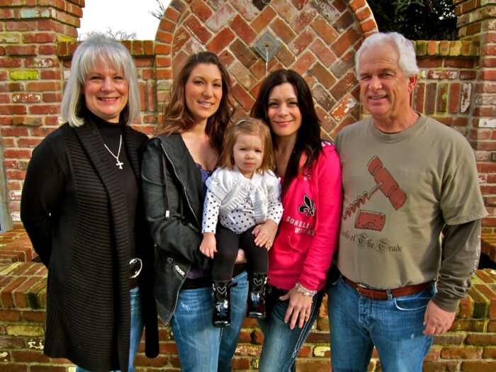 Family group smiling outdoors in front of brick wall, enjoying Lodi wine region experience.