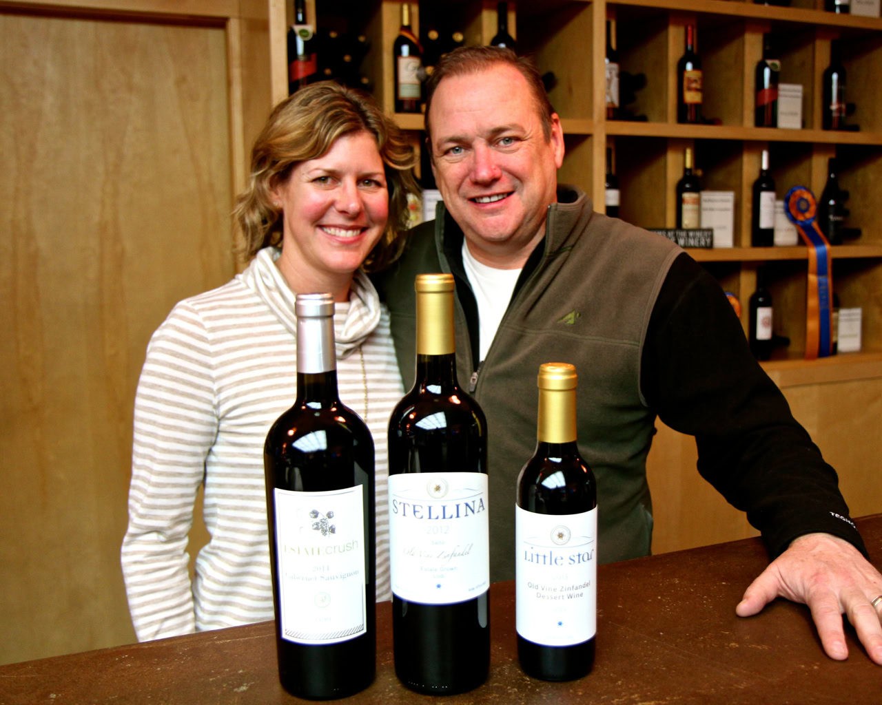 Two people smiling at a wine tasting event with bottles of wine from Lodi Winegrape Commission.