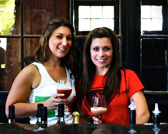 Two women enjoying wine tasting at Lodi Winegrape Commission event, holding glasses of rosé wine.