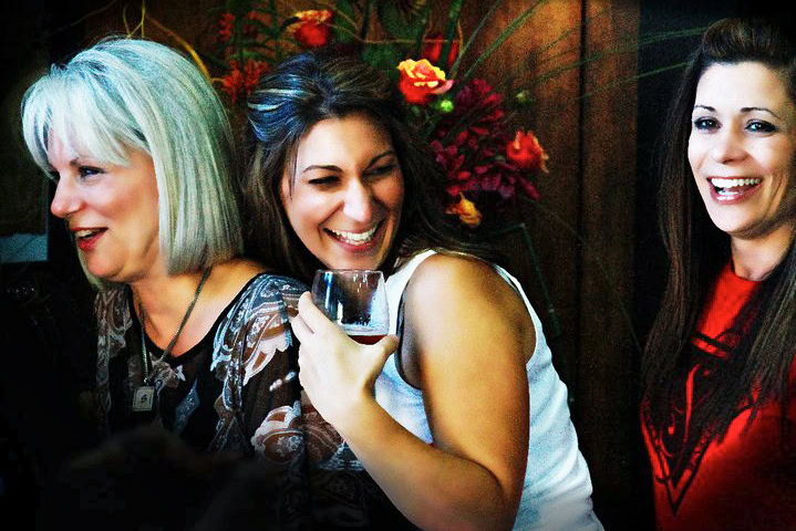 Women enjoying wine at a Lodi Winegrape Commission event, smiling and socializing with a floral background.
