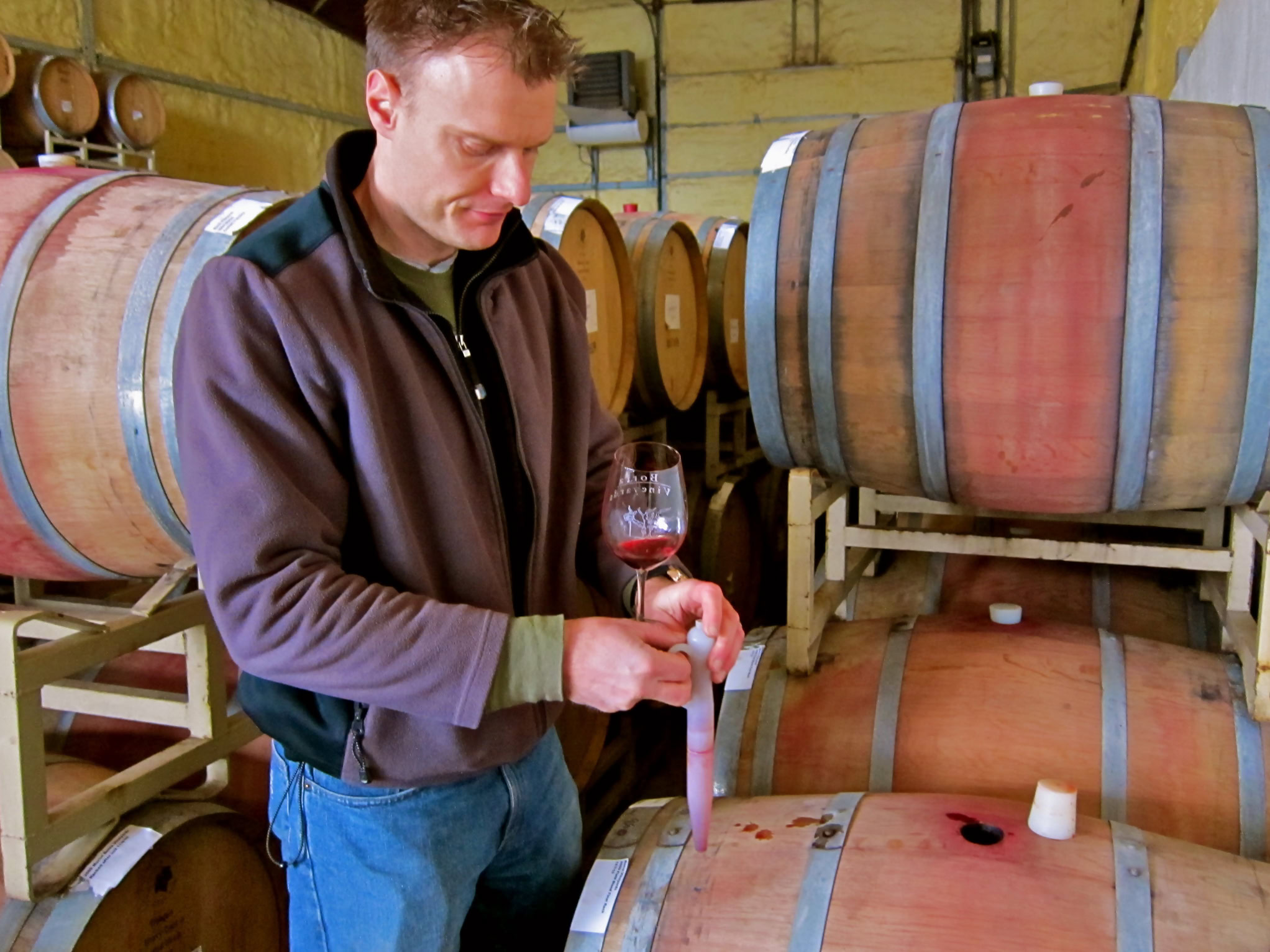 Man tasting wine in a winery with wine barrels in the background.