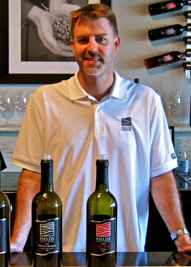 Man at wine tasting event with wine bottles and glasses, promoting Lodi winegrapes and local wine industry.