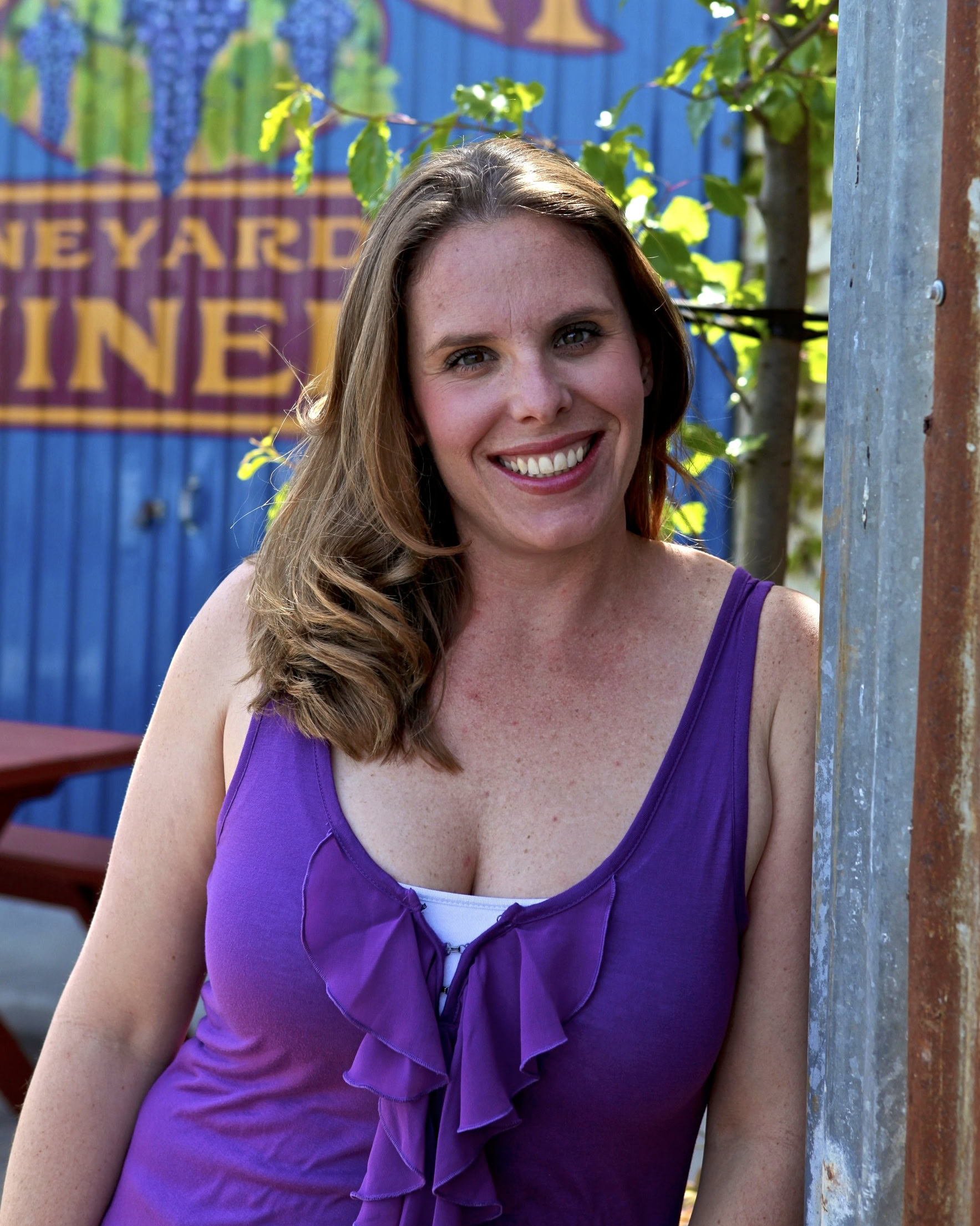 Smiling woman in purple top at Lodi Winegrape Commission event, vineyard background, sunny day.