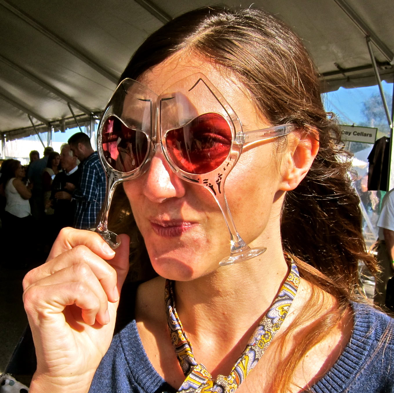 Woman tasting wine at Lodi Winegrape Commission event with sunglasses and festival setting.