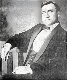 Black and white portrait of a man in formal suit with bow tie, seated confidently.