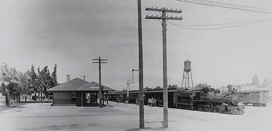 Black and white photo of a vintage train station with train cars and water tower in Lodi, California.