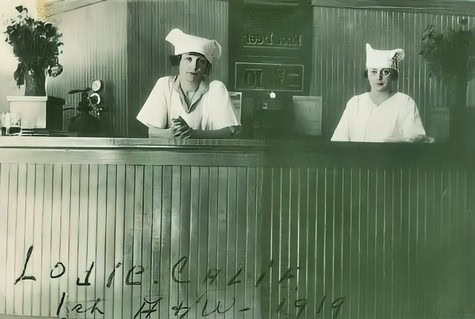 Two nurses in vintage uniforms sitting behind a wooden counter at Lodi Winegrape Commission.