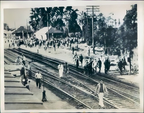 Black and white photo of a busy train station with people and tracks from the early 20th century.