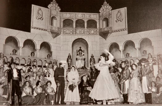 Vintage black and white photo of a theatrical opera performance with actors in period costumes on stage.