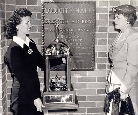Historical black and white photo of two women exchanging a trophy in front of Lodi City Hall.