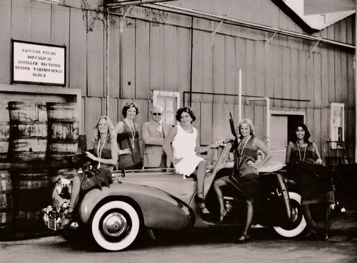 Group of women and a man with a vintage car outside a barn, celebrating Lodi wine industry history.