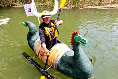 Person in Viking hat paddling a dragon-shaped float in a waterway during a Lodi Winegrape Commission event.