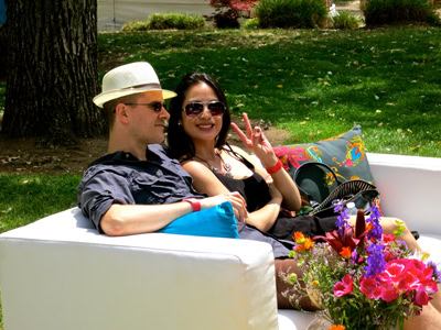 Two people relaxing on a white sofa outdoors, with colorful flowers and greenery in the background.