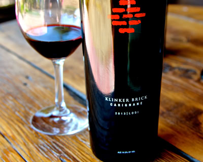 Close-up of Klinker Brick Carignane wine bottle and glass of red wine on wooden table.