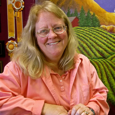 Smiling woman in pink shirt in front of Lodi Winegrape Commission mural.