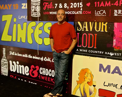 Man in red shirt standing in front of colorful wine event banners at Lodi Wine event.