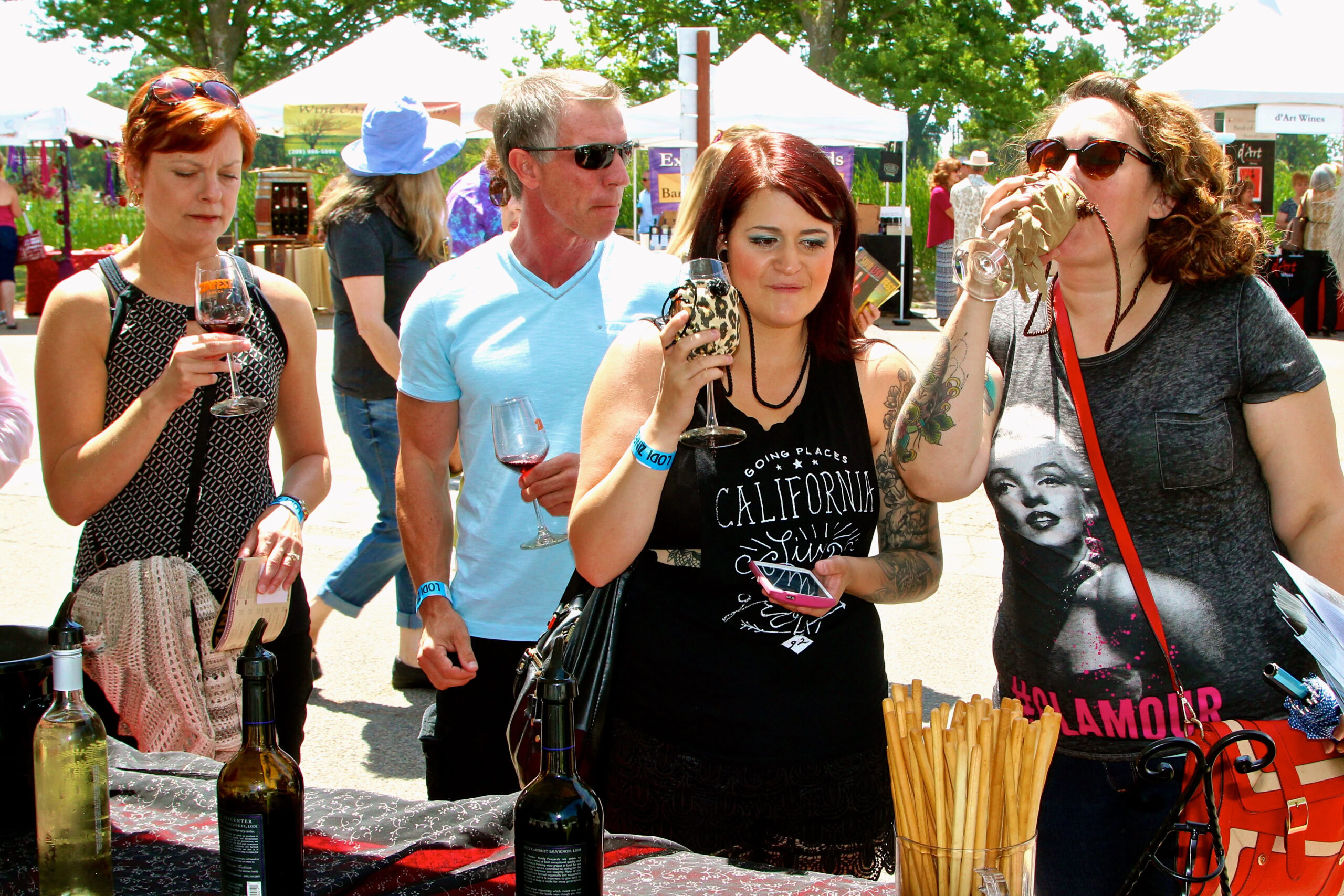 People tasting wine at the Lodi Winegrape Commission outdoor event in sunny weather.