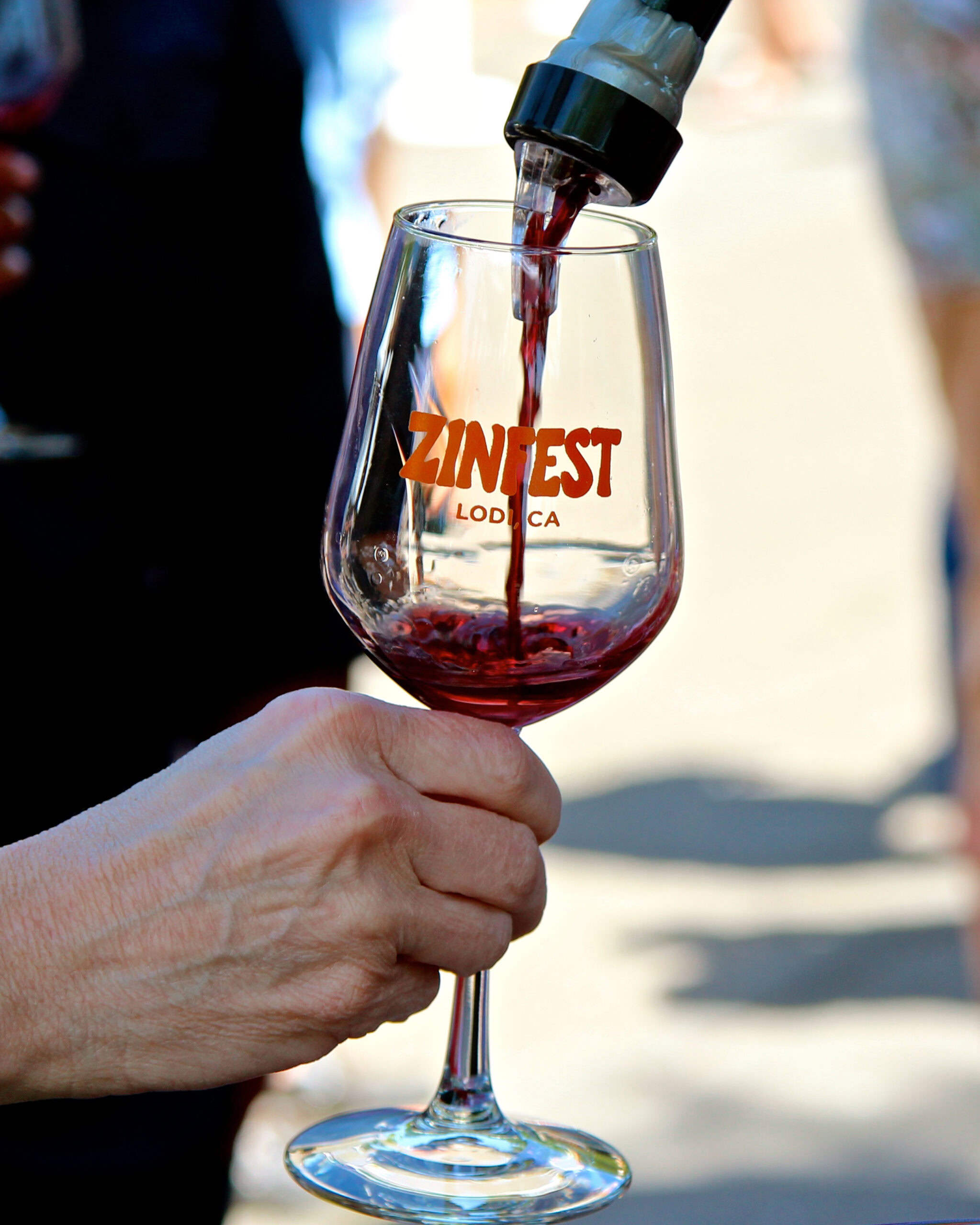 Pouring red wine into a glass with Lodi Winegrape Commission logo during wine tasting event.