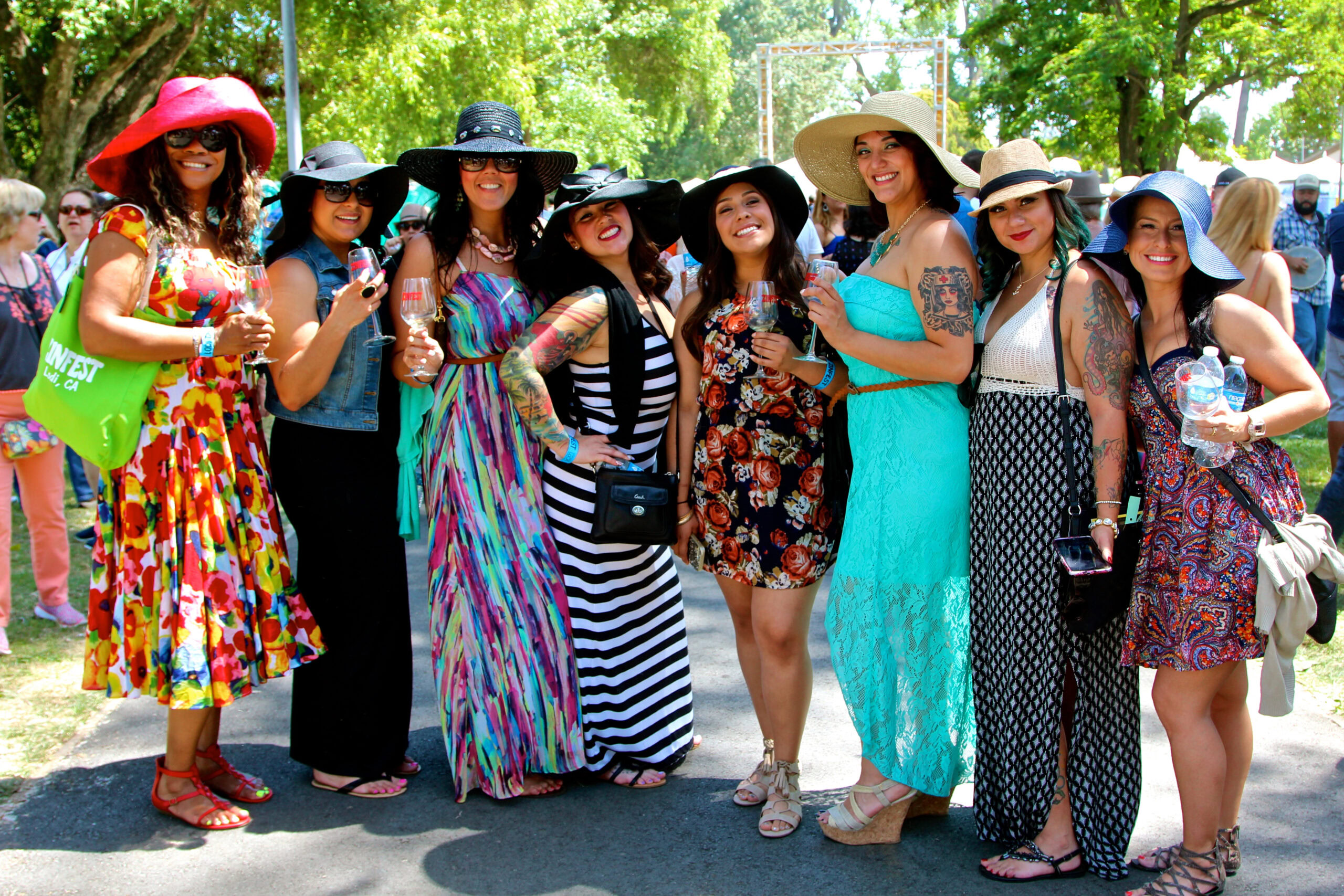 Group of women at Lodi Winegrape Commission event wearing colorful dresses and hats outdoors.