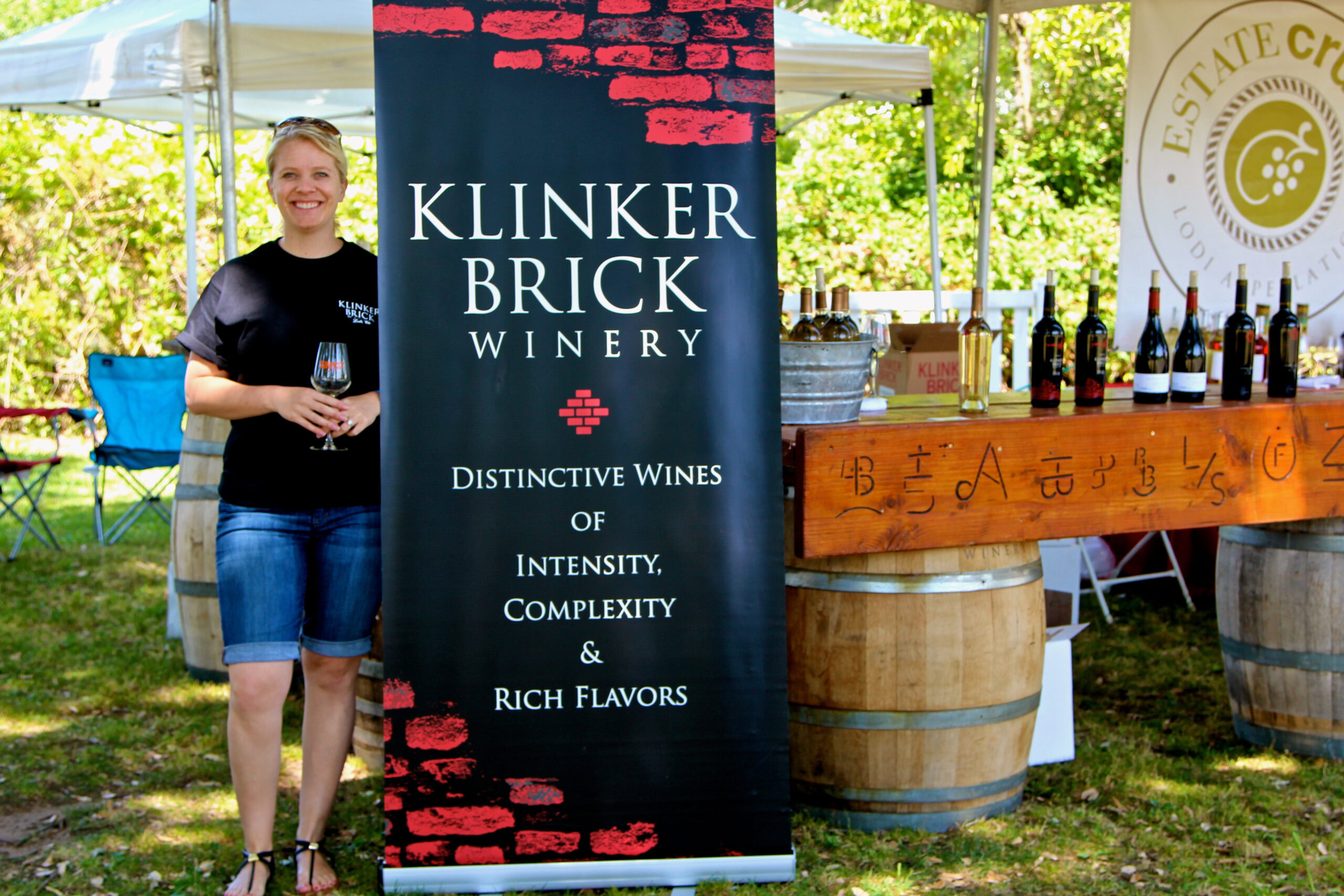 Woman holding a glass of wine at a wine tasting event with Klinker Brick Winery banner in the background.