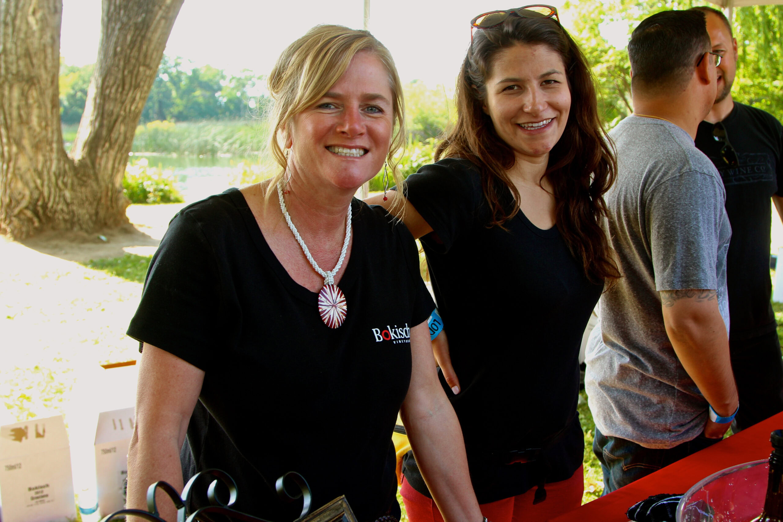Smiling women at Lodi Winegrape Commission outdoor event with trees and water in background.