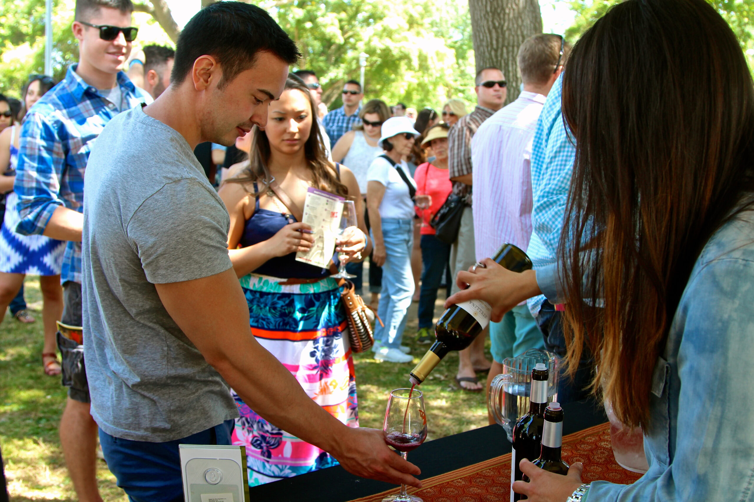 People enjoying wine tasting outdoors at Lodi Winegrape Commission event in a park setting.