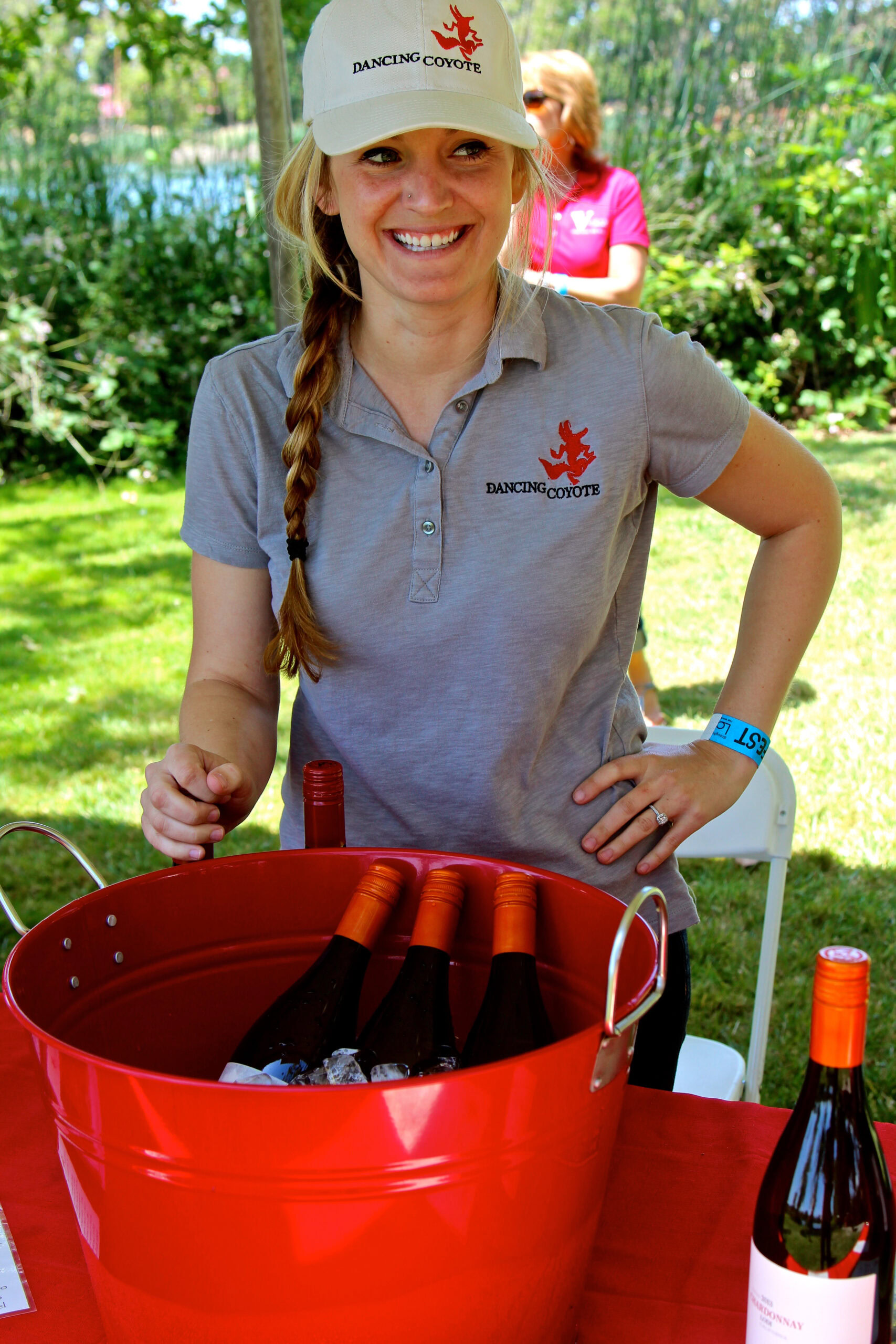 Smiling woman at Lodi Winegrape Commission event with wine bottles in a red bucket.