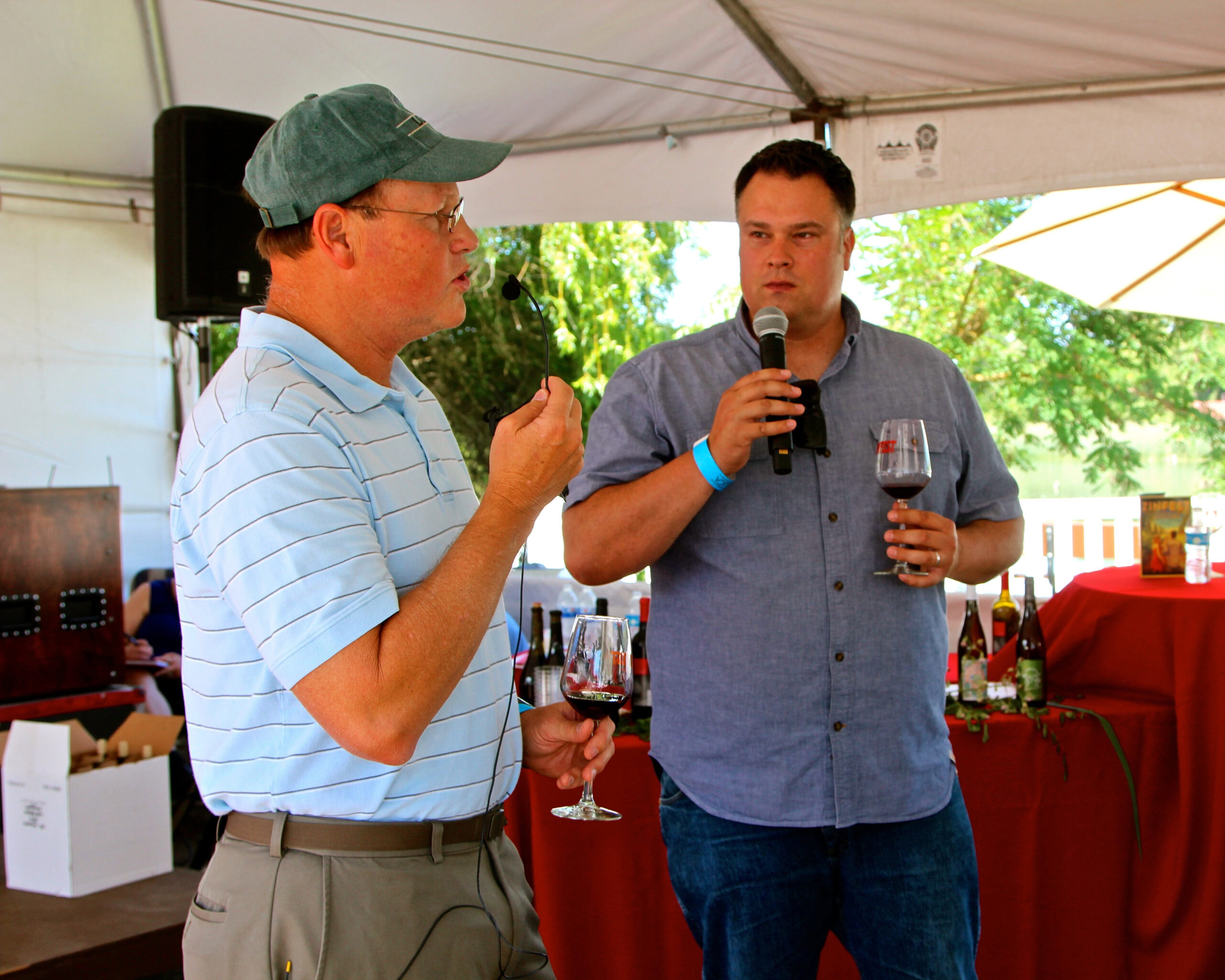 Two men tasting wine at a Lodi Winegrape Commission event with a microphone and wine glasses.