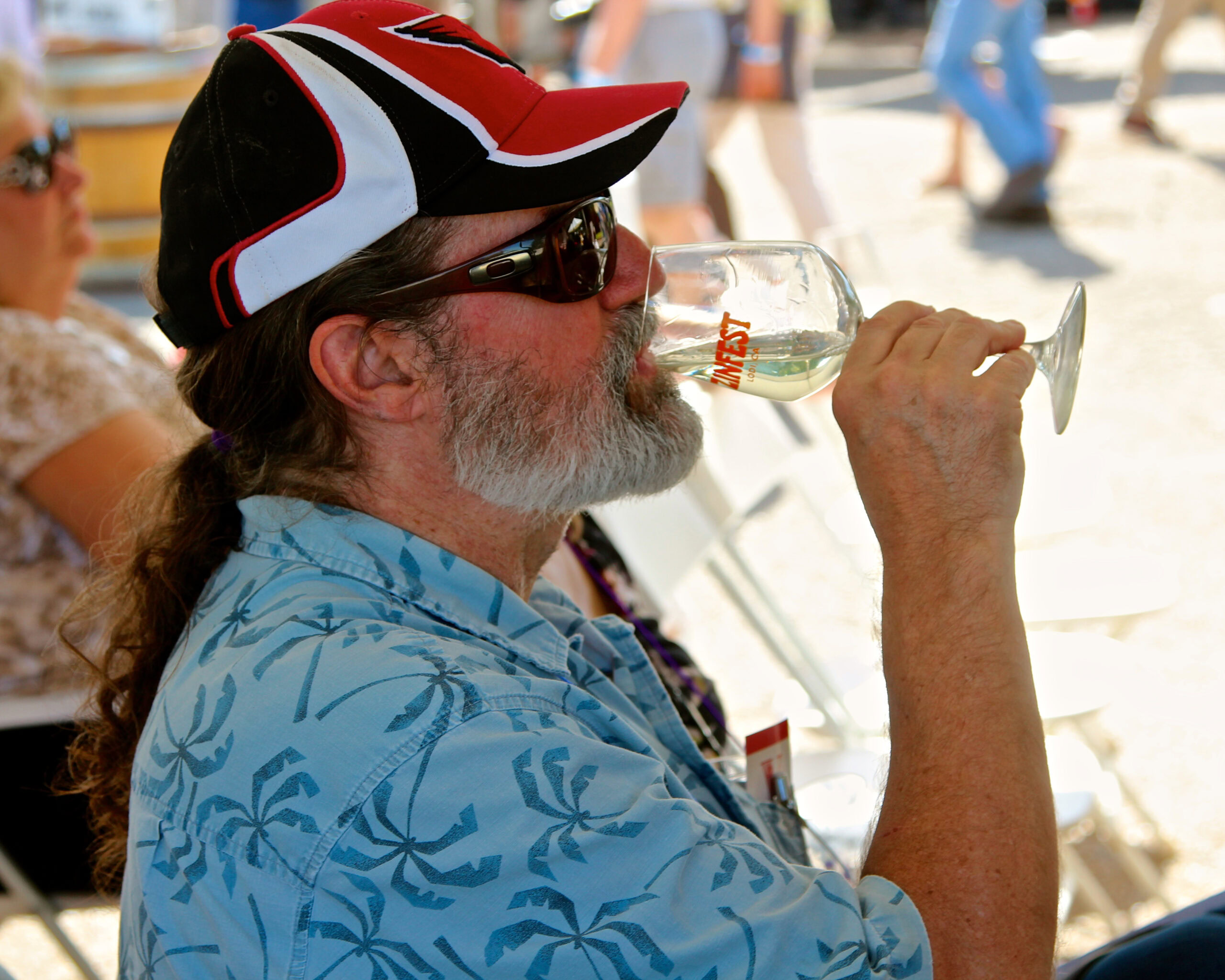 Man enjoying wine at Lodi Winegrape Commission event, wearing sunglasses and a cap, with a glass of white wine.