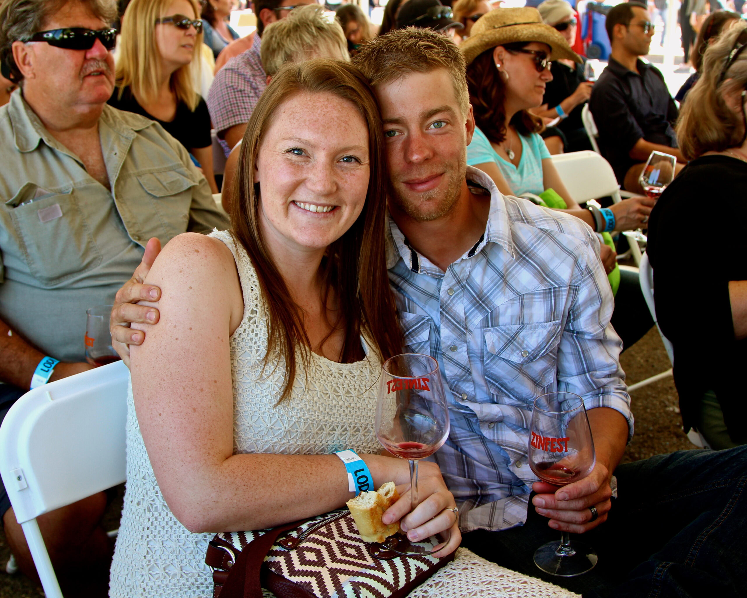 Smiling couple enjoying wine tasting at Lodi Winegrape Commission event with crowd in background.
